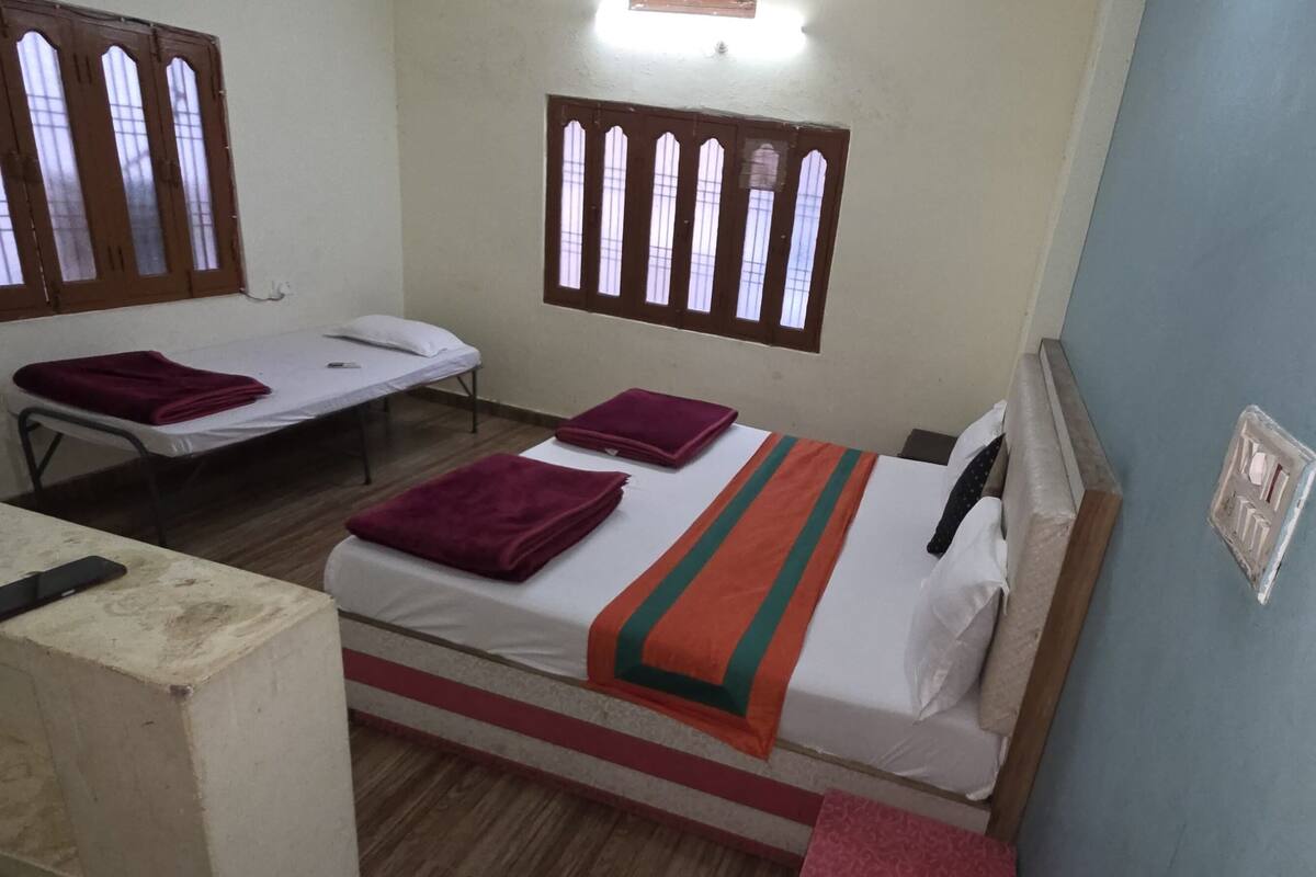 Une chambre avec deux lits, chacun équipé d’un oreiller et d’une couverture. Il y a deux fenêtres avec des cadres en bois et des vitres.