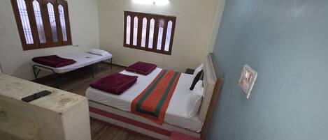A room with two beds, each with a pillow and a blanket. There are two windows with wooden frames and glass panes.