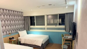 A hotel room with two beds, a desk with a chair, a TV, and a window with curtains. - Ximenhotel Xining (Taipei)