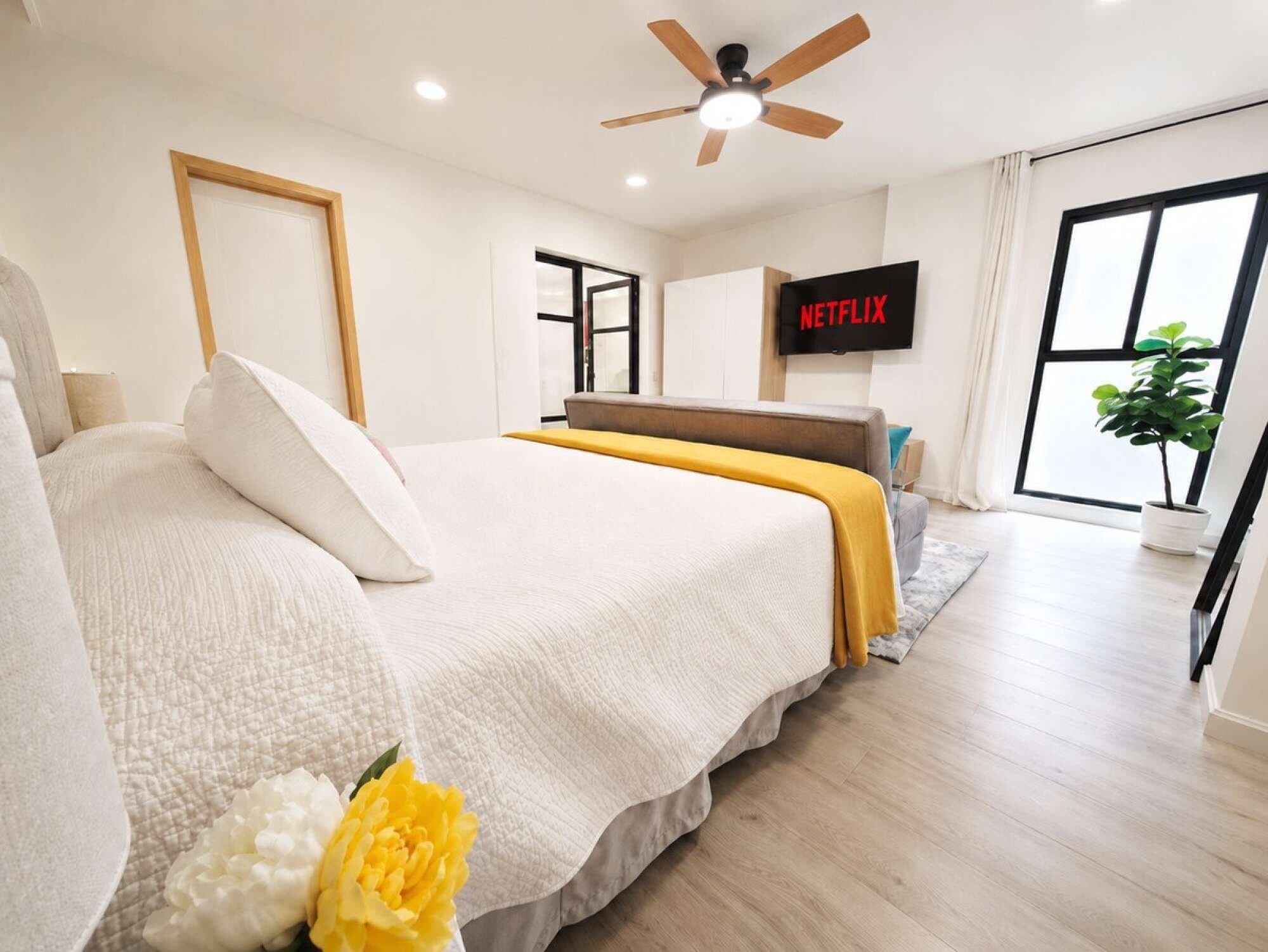 A modern bedroom with a bed, a ceiling fan, a television, and a large window.