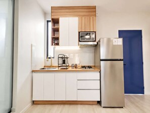 A compact kitchen with white cabinets, a stainless steel refrigerator, a microwave, and a gas stove. - Coco 8 · 30 m² suite with terrace in Condesa · 1 bath (Mexico City)