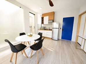 Eine moderne Küche mit weißen Schränken, einer Mikrowelle und einem Kühlschrank. Es gibt einen Essbereich mit einem weißen Tisch und schwarzen Stühlen.
