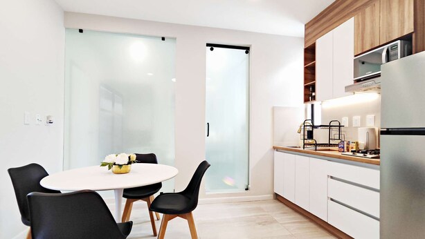 A modern kitchen with white cabinets, a stainless steel refrigerator, and a dining area with a round table and black chairs. - Stay in Condesa | New, Cozy & Full of Charm (Mexico City)