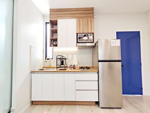 A compact kitchen with white cabinets, a stainless steel refrigerator, a built-in microwave, and a wooden countertop. - Stay in Condesa | New, Cozy & Full of Charm (Mexico City)