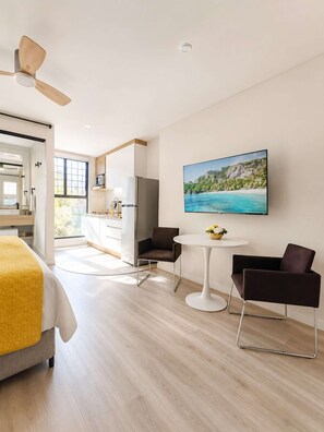A modern hotel room with a bed, a dining area with a table and chairs, a kitchen area, and a large window with a view of a beach. - Coco 4 · 20 m² studio with terrace in Condesa · 1 bath (Mexico City)