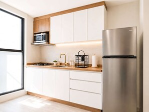 A modern kitchen with a built-in microwave, stainless steel refrigerator, and wooden cabinets. - Coco 4 · 20 m² studio with terrace in Condesa · 1 bath (Mexico City)