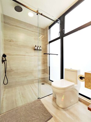 A modern bathroom with a glass-enclosed shower, a toilet, and a large window providing natural light. - Coco 4 · 20 m² studio with terrace in Condesa · 1 bath (Mexico City)