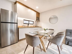 A modern kitchen with a stainless steel refrigerator, a microwave, and a window above the sink. There is a dining area with a glass table and four chairs. - Coco 3 · 40 m² suite with balcony and terrace · 1 bath (Mexico City)