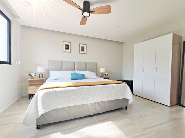 Quarto moderno com uma cama grande, duas mesas de cabeceira com luminárias, um ventilador de teto e um guarda-roupa.
