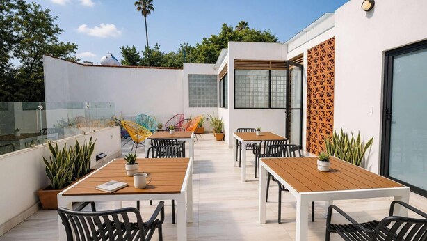 A rooftop terrace with outdoor seating, potted plants, and a modern building with geometric wall design. - Modern Condesa 1BR | King & Sofa Bed | Brand New (Mexico City)