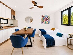 Quarto de hotel moderno com área de refeições, ventilador de teto, espelho grande e uma obra de arte colorida na parede.