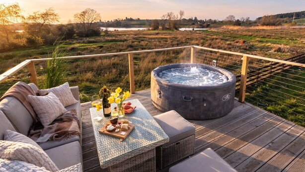 A hot tub on a deck with a view of a lake and trees. - Waterside Cabin | Cavan Lakes | Hot Tub (CN)