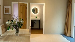 A room with a wooden dining table, a vase of flowers, a mirror above a sink, and a door leading to a bathroom. - Waterside Cabin | Cavan Lakes | Hot Tub (CN)