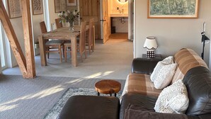 A spacious living room with a wooden ceiling, a leather sofa, a dining area with wooden chairs, and a kitchen visible through an open door. - Waterside Cabin | Cavan Lakes | Hot Tub (CN)