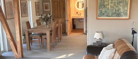 A spacious living room with a wooden ceiling, a leather sofa, a dining area with wooden chairs, and a kitchen visible through an open door.