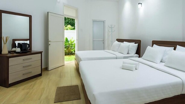 Une chambre d’hôtel avec deux lits, une commode en bois, un miroir et une porte donnant sur un balcon.