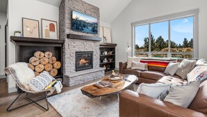 A modern living room with a stone fireplace, a large window with a view, and a cozy seating area. - Brasada Ranch Elegance | Hot Tub| Bocce| Ping Pong (Powell Butte)