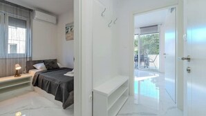 Une chambre moderne avec un lit, une table de chevet et un banc. Une porte donne accès à un balcon avec une piscine.