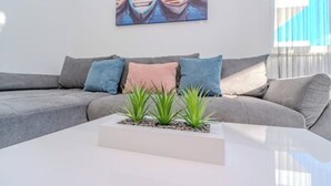 Un salon moderne avec un canapé d’angle gris, une table basse blanche et un tableau représentant des bateaux accroché au mur.