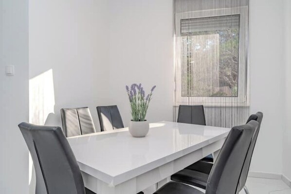 Une salle à manger moderne avec une table blanche, six chaises et une plante en pot.