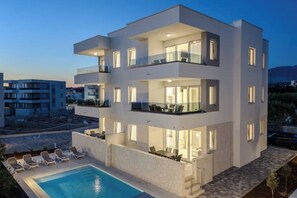 Un immeuble moderne à plusieurs étages, doté de balcons, d’une piscine et d’un espace de détente extérieur.