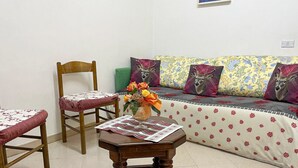 A room with a wooden chair, a small table with a vase of flowers, and a sofa with patterned cushions. - Casa vacanze - Villa Stefania 1 (Pescocostanzo)