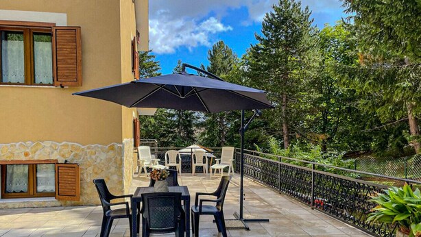 An outdoor patio with a table and chairs, a large umbrella, and a stone wall. - Casa vacanze - Villa Stefania 1 (Pescocostanzo)