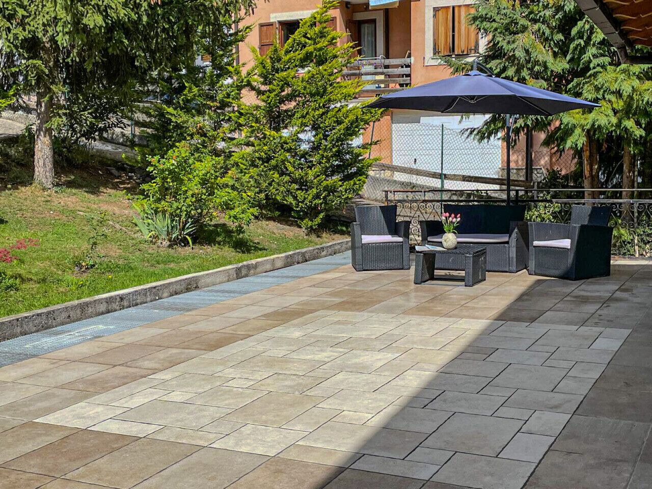Une terrasse extérieure avec un sol carrelé, des meubles en osier et un parasol bleu.