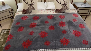 Un letto con due cuscini decorati con immagini di cervi, una coperta grigia con motivi floreali rossi e una federa coordinata.