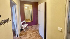 A hallway with a wooden floor, a white chair, a white wardrobe, and a mirror with a gold frame.