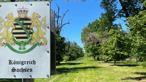 A sign with a coat of arms and the text 'Königreich Sachsen' in a park setting.