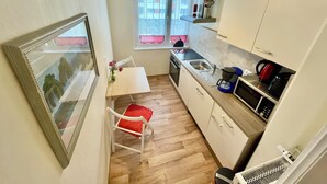 A compact kitchen with a dining area, a window with curtains, and a small table with a chair.