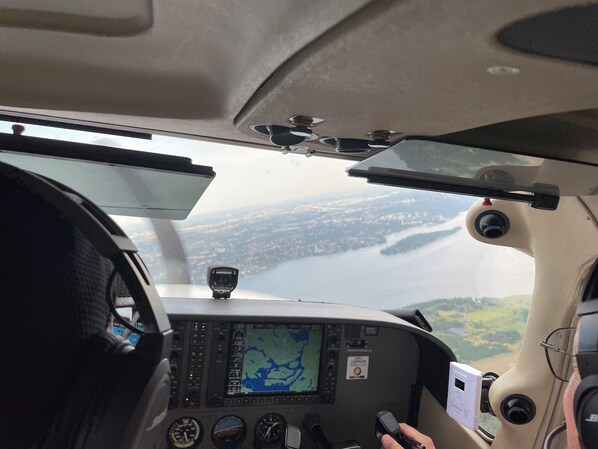 Vista desde la cabina con panel de control de vuelo, pantalla de mapa y una vista de agua y tierra abajo.