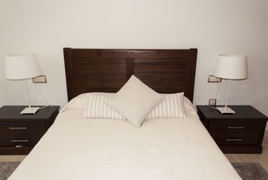 A neatly made bed with a wooden headboard, two bedside tables with lamps, and a small drawer. - Central location, parking, next to the train (Cordoba)