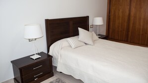 A neatly made bed with white bedding, a dark wooden headboard, and two bedside tables with lamps. - Central location, parking, next to the train (Cordoba)
