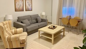 A living room with a sofa, striped armchair, coffee table, and a dining area with chairs and a table. - Central location, parking, next to the train (Cordoba)