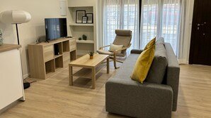 A modern living room with a grey sofa, a wooden coffee table, a TV on a wooden stand, and a chair with a cushion. - Downtown Loft 16A Córdoba (Cordoba)