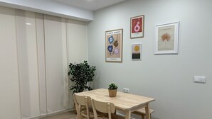 Ein Zimmer mit einem Holztisch, Stühlen, einer Topfpflanze und drei gerahmten Bildern an der Wand.