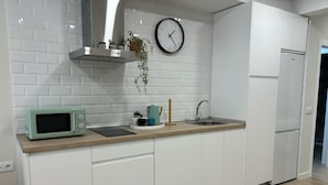 Eine moderne Küche mit weißen Schränken, einer Mikrowelle, einem Spülbecken und einer Uhr an der Wand.
