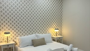 Ein ordentlich eingerichtetes Schlafzimmer mit Wandmuster, zwei Nachttischlampen, einem Bett mit grauer Decke und einem Deckenventilator.