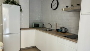 Eine moderne Küche mit weißen Schränken, einer Mikrowelle, einem Spülbecken, einer Uhr und einer Pflanze auf dem Kühlschrank.