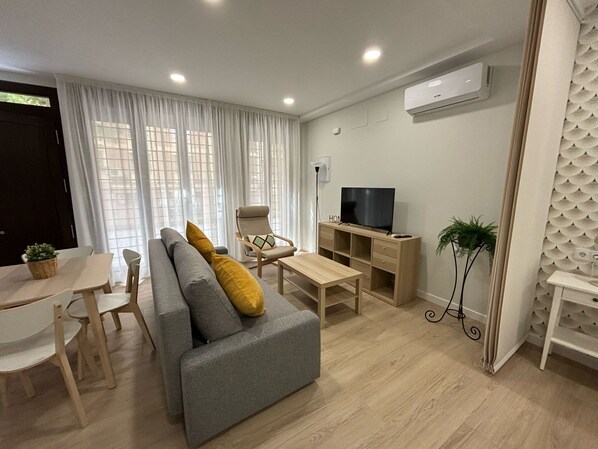 Una sala moderna con un sofá gris, una mesa de centro de madera y un mueble para televisión.