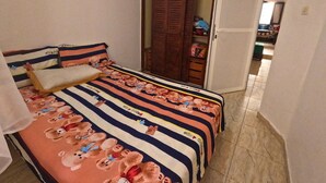 A bedroom with a bed featuring a striped bedspread with cartoon characters, a wooden wardrobe, and a door leading to another room. - Beach 2 minutes away - Quiet and ideal for families (M'diq)