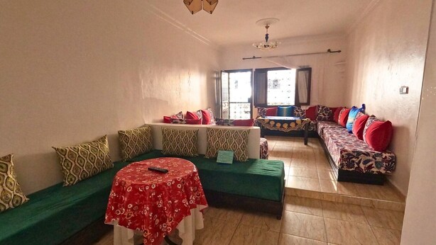 A living room with green sofas, a round table with a red tablecloth, and a patterned sofa with red cushions. - Beach 2 minutes away - Quiet and ideal for families (M'diq)