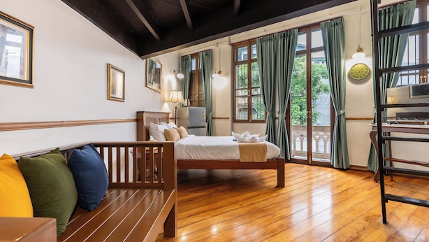 Habitación de hotel con piso de madera, una cama con almohadas, un banco, un escritorio con lámpara y vistas a zonas verdes.