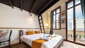 Habitación de hotel con cama, una silla, una escalera, un ventanal y vistas al exterior.