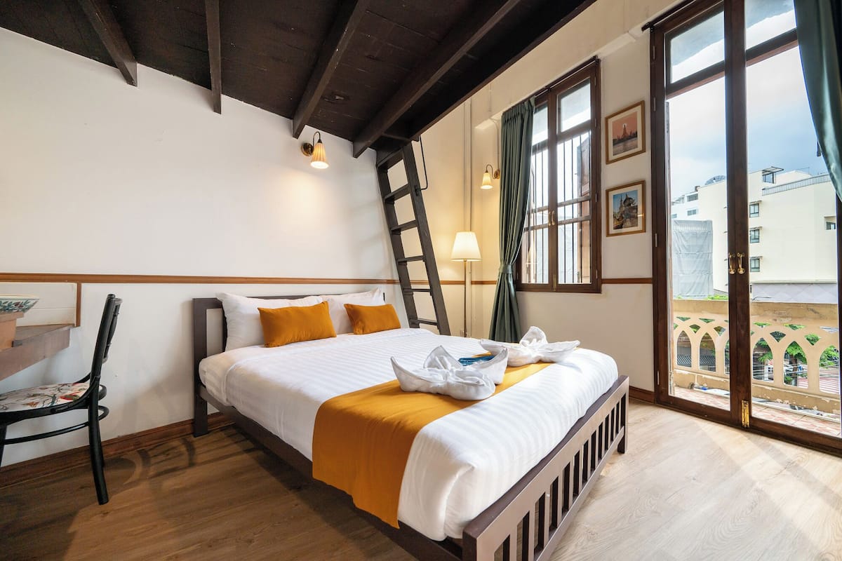 Een hotelkamer met een bed, een stoel, een ladder, een raam en uitzicht.