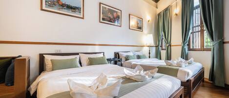 Habitación de hotel con tres camas, cabeceras de madera y un ventanal con cortinas.