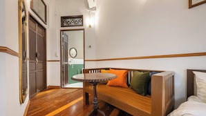Una habitación con un banco de madera, una pequeña mesa redonda y una cama con ropa de cama blanca.