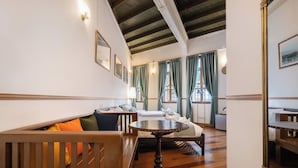 Habitación de hotel con un banco de madera, una mesa redonda y una cama con cabecera blanca.